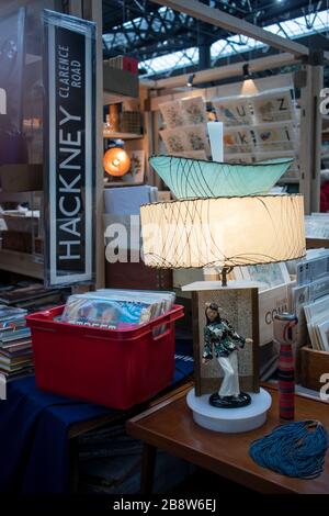 Londra, Regno Unito - 13 febbraio 2020 Spitalfields mercato delle pulci. Lampada da tavolo Art Nouveau e statuina cinese. Piastre in una scatola di plastica. Foto Stock