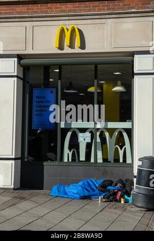 Windsor, Berkshire, Regno Unito. 23 marzo 2020. McDonald's Restaurants nel Regno Unito hanno annunciato che chiuderanno tutti i loro 1270 ristoranti alla fine di oggi a causa dell'esclamazione del Coronavirus Pandemic nel Regno Unito. Un senzatetto dorme fuori dal ristorante prima che chiuda temporaneamente. Credit: Maureen McLean/Alamy Live News Foto Stock