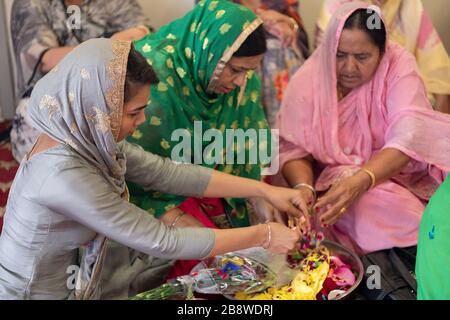 Devout Sikh donne di diverse età rompere di petali di fiori da utilizzare in un servizio mattutino. Al Centro Culturale Sikh a South Richmond Hill, Queens. Foto Stock