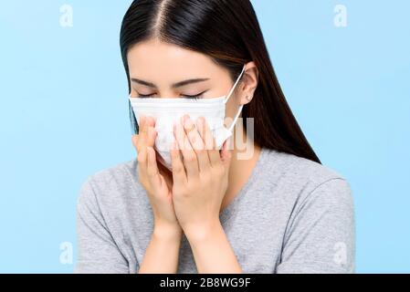 Donna asiatica che indossa la maschera medica tosse isolato su sfondo azzurro chiaro Foto Stock