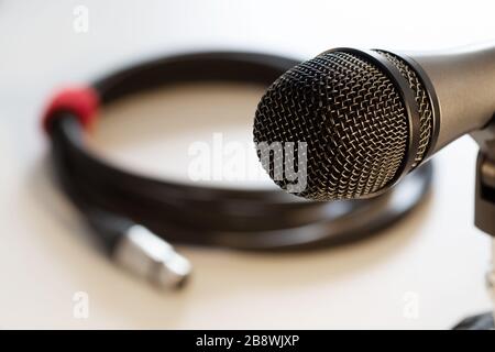 Primo piano della testa del microfono vocale con griglia nera e cavo con connettore xlr in background isolato su bianco. Musica, audio, hi-fi, karaoke e sostantivo Foto Stock