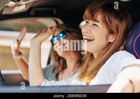 Felice entusiasta bella giovane donna che agita con le mani durante la guida in auto Foto Stock