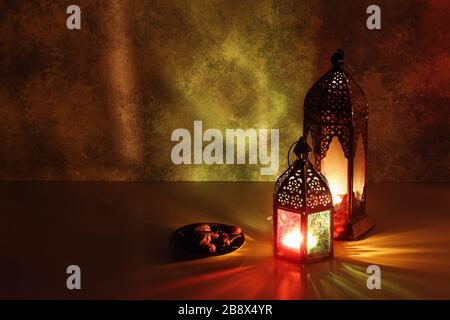 Lanterne arabe ornamentali e piatto con frutta dattera. Le candele bruciate sul tavolo si illuminano di notte. Biglietto d'auguri per le feste, invito per il Santo mon musulmano Foto Stock