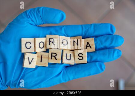 Una mano con un guanto su sostiene mattoni Scrabble, che formano la parola: Corona Virus Foto Stock