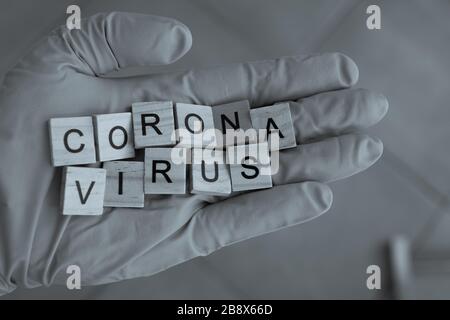 Una mano con un guanto su sostiene mattoni Scrabble, che formano la parola: Corona Virus Foto Stock