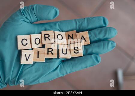 Una mano con un guanto su sostiene mattoni Scrabble, che formano la parola: Corona Virus Foto Stock