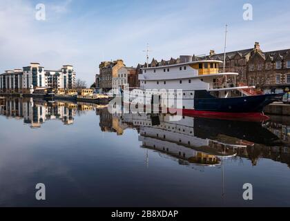 The Shore, Leith, Edimburgo, Scozia, Regno Unito. 23 marzo 2020. UK Weather: Il sole primaverile e la brezza creano un perfetto riflesso dei vecchi edifici e chiatte nell'acqua di Leith lungo la riva deserta del fiume, mentre la gente rimane a casa a distanza sociale Foto Stock