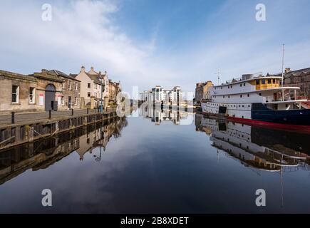 The Shore, Leith, Edimburgo, Scozia, Regno Unito. 23 marzo 2020. UK Weather: Il sole primaverile e la brezza creano un perfetto riflesso dei vecchi edifici e chiatte nell'acqua di Leith lungo la riva deserta del fiume, mentre la gente rimane a casa a distanza sociale Foto Stock