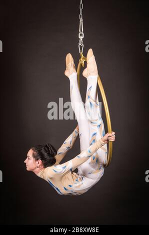 Una donna snella, dai capelli scuri - un acrobata d'aria in un vestito bianco e blu, esegue esercizi in un anello d'aria. Riprese in studio su sfondo scuro. Foto Stock