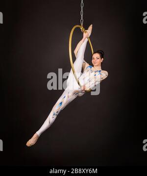 Una donna snella, dai capelli scuri - un acrobata d'aria in un vestito bianco e blu, esegue esercizi in un anello d'aria. Riprese in studio su sfondo scuro. Foto Stock