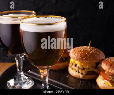 Birra fredda in un bicchiere e uno spuntino sotto forma di grandi hamburger succosi. Fast food. Foto Stock