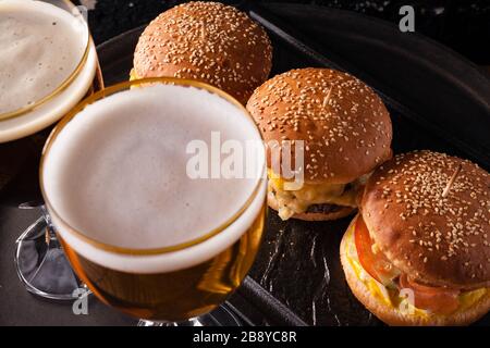 Birra fredda in un bicchiere e uno spuntino sotto forma di grandi hamburger succosi. Fast food. Foto Stock