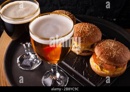 Birra fredda in un bicchiere e uno spuntino sotto forma di grandi hamburger succosi. Fast food. Foto Stock