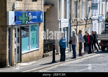 Le persone si accodano al di fuori di una farmacia Boots nel Somerset, poiché le misure di distanza sociale hanno effetto in tutto il Regno Unito per cercare di combattere l'epidemia di Coronavirus. Foto Stock