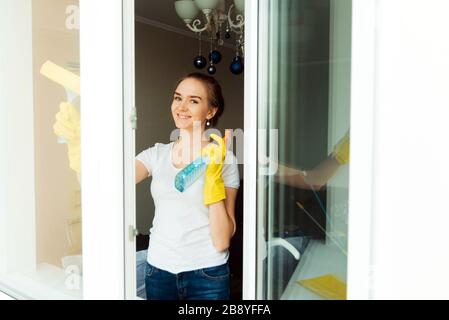 Un adulto carino donna pulizia impresa lavoratore salviette finestre di plastica in una casa. La vista dall'esterno. Foto Stock