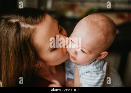 Una mamma tiene un bambino tra le braccia. Una madre bacia un bambino. Una giovane donna abbraccia il suo bambino. Una ragazza ha divertimento e gioisce con il baby.Close up. Foto Stock