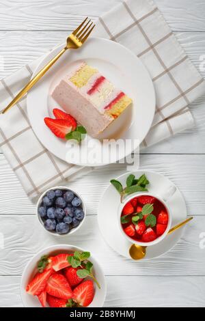 una fetta di cheesecake rosa alla fragola servita con bacche fresche e limonata di fragole in una tazza su un tavolo di legno, vista verticale dall'alto Foto Stock