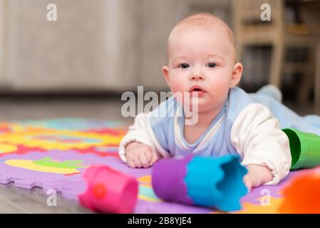 Un bambino gioca sul pavimento. Il bambino è sdraiato sulla sua pancia sul tappeto con una piramide. Foto Stock