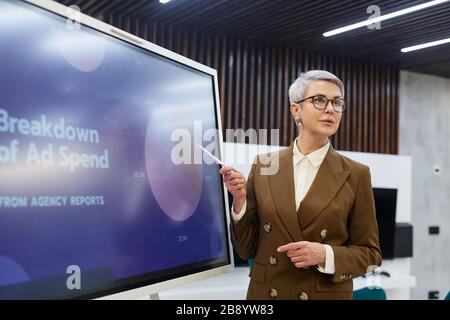 Vita su ritratto di successo maturo businesswoman che punta al grafico della torta mentre dà la presentazione sull'introduzione sul mercato, spazio della copia Foto Stock