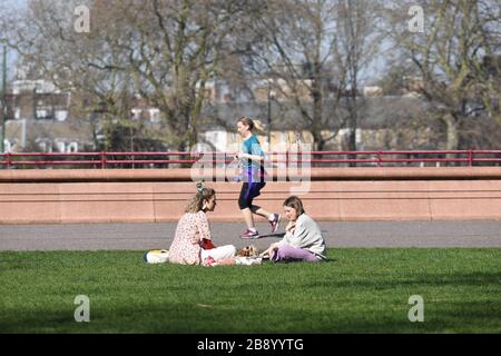 Una donna scherza davanti a due donne che socializzano a Battersea Park, Londra, come ha detto il primo ministro Boris Johnson, il governo è pronto ad imporre restrizioni più severe per frenare la diffusione del coronavirus se la gente non segue le linee guida sulle distanze sociali. Foto Stock