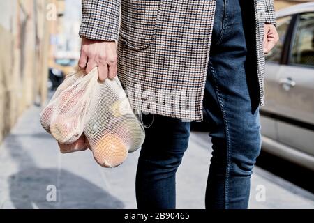 closeup di un uomo sulla strada che trasporta alcuni sacchetti di maglia riutilizzabili tessili, usati per comprare i generi alimentari alla rinfusa, pieni di frutta e verdura, come misura a. Foto Stock