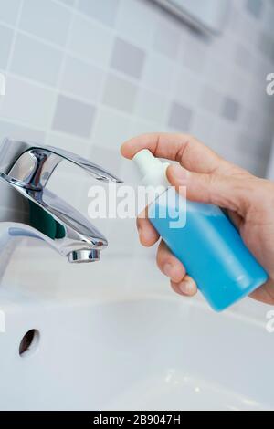 closeup di un uomo caucasico disinfettando il rubinetto di un lavandino spruzzando un disinfettante blu da una bottiglia Foto Stock