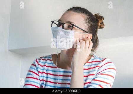 Primo piano di una giovane donna in una maschera chirurgica sul viso contro SARS-cov-2. Quarantena e isolamento a casa a causa del virus influenzale coronavirus. Femmina malata Foto Stock