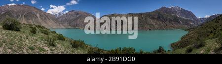 Panorama del verde azzurro lago di Iskanderkul a Tadzjikistan con alte montagne innevate. Foto Stock