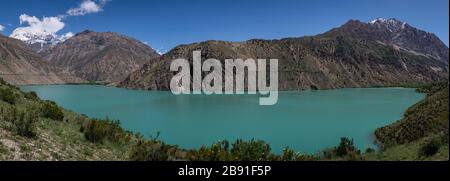 Panorama del verde azzurro lago di Iskanderkul in Tazjikistan con alte montagne innevate. Foto Stock