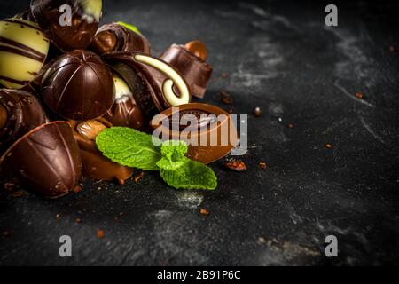 Varie caramelle al cioccolato su sfondo scuro. Diversi dolci e cioccolatini con foglie di menta, spazio per la copia Foto Stock