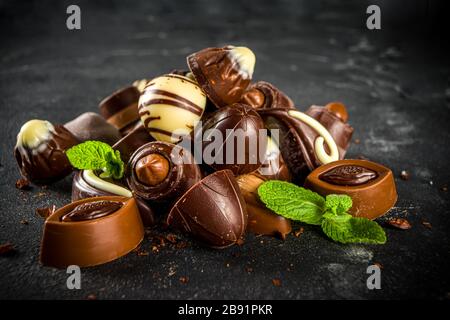 Varie caramelle al cioccolato su sfondo scuro. Diversi dolci e cioccolatini con foglie di menta, spazio per la copia Foto Stock