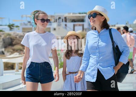 Madre a piedi con due figlie in mano nel famoso villaggio turistico Oia Santorini isola. Felice donna e ragazze in estate sole giorno a piedi toget Foto Stock