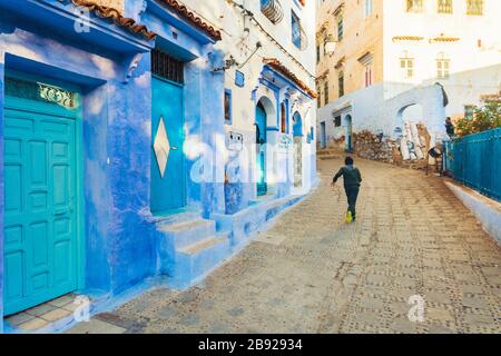 Ragazzo locale che corre per la strada di Chefchaouen blu villaggio Foto Stock