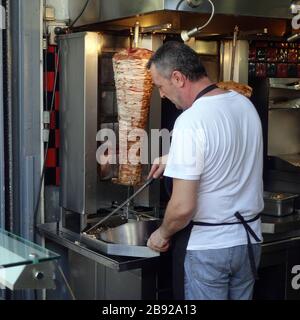 Atene, Grecia - 14 settembre 2019: Uomo affettando pezzi di carne per souvlaki da giros rotisserie macchina. Foto Stock