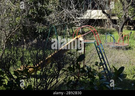 Altalene scivoli e allegro andare in giro in abbandonati overgrown parco giochi per bambini. Foto Stock