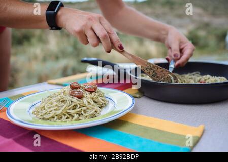 Primo piano delle mani della donna che prepara la pasta con il pesto durante un viaggio. Foto Stock