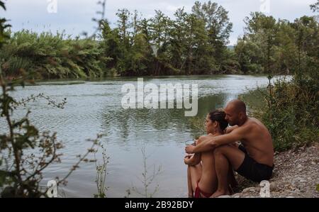 Coppia in costumi da bagno abbracciando da una riva del fiume durante una vacanza. Foto Stock