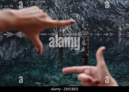 Mani di donna non focalizzate che incorniciano alcuni alberi in un paesaggio di montagna. Foto Stock