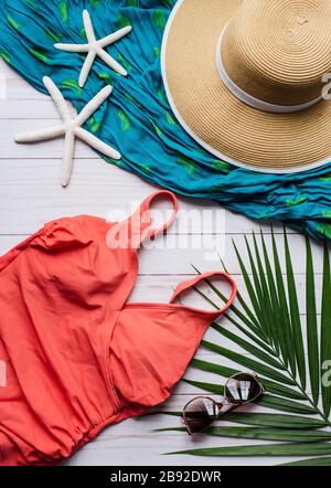 Vista dall'alto del costume da bagno e degli accessori da spiaggia su sfondo di legno bianco. Foto Stock