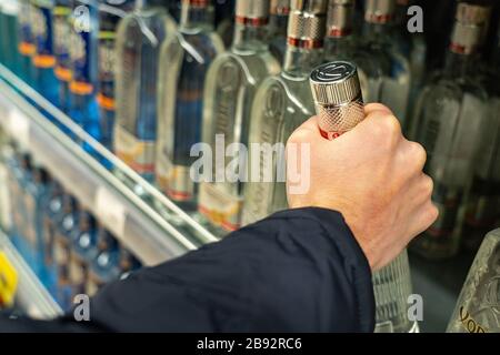 Ekaterinburg, Russia - Novembre 2019. Una bottiglia di vodka di marca Khortytsa è tenuta in una mano maschile. File di bottiglie nel reparto alcool del Foto Stock