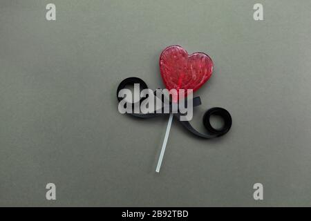 Creative Flat Lay con un cuore rosso Lollipop a forma di cuore con un arco nero per San Valentino Foto Stock