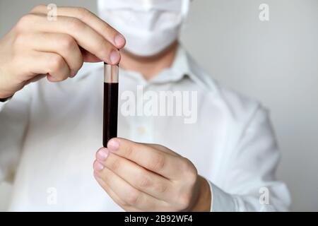 Test per coronavirus, primo piano provetta in mano maschile. Uomo in maschera medica contenente un flaconcino con liquido rosso, concetto di campione di sangue di covid-19, vaccinazione Foto Stock