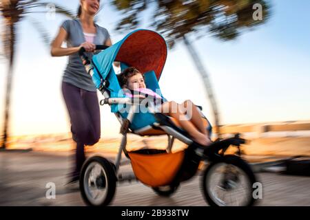 Donna che fa jogging mentre spinge la figlia in un passeggino. Foto Stock