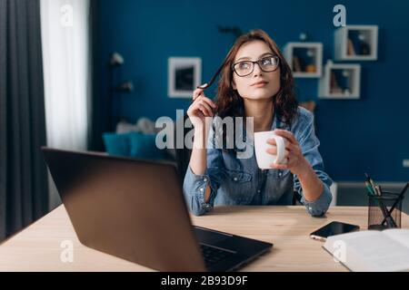 Bella donna seduta in piano con computer portatile e bere caffè Foto Stock