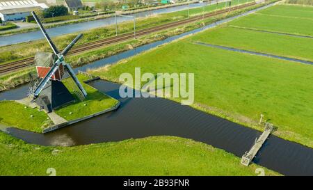 Veduta aerea di un vecchio mulino tradizionale olandese a vento sulla campagna nei Paesi Bassi con una diga, canali, ferrovia, ponte e una strada. Foto Stock