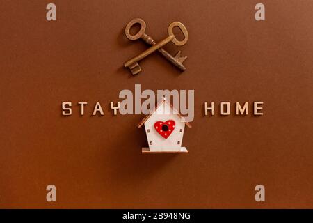 Le parole rimangono a casa fatte da lettere di legno, figure di casa e chiavi, concetto di auto quarantena a casa come misura preventiva contro il virus corona Foto Stock
