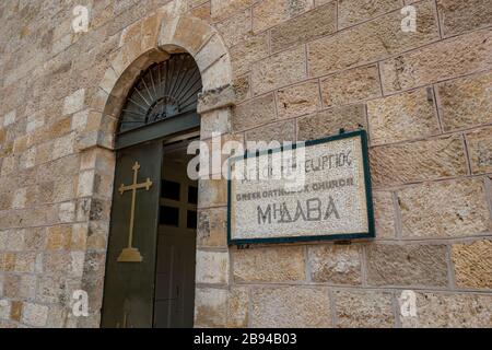 La bella targa a mosaico all'ingresso della chiesa greco ortodossa di San Giorgio a Madaba, Giordania. Vista sulla strada durante il giorno d'inverno con la vecchia porta aperta dell'edificio religioso Foto Stock