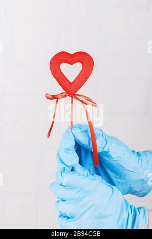 Mano femminile in guanti blu per uso medico che tengono un cuore rosso, simbolo di vita. Concetto di sostegno di persone infettate di coronavirus, proteggere e difend il Foto Stock