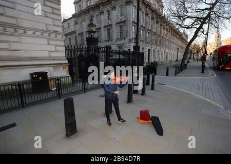 Un uomo gioca il violino fuori Downing Street in una Whitehall vuota, Londra, come il primo ministro Boris Johnson ha detto che il governo è pronto ad imporre restrizioni più severe per frenare la diffusione del coronavirus se la gente non segue le linee guida sulle distanze sociali. Foto Stock