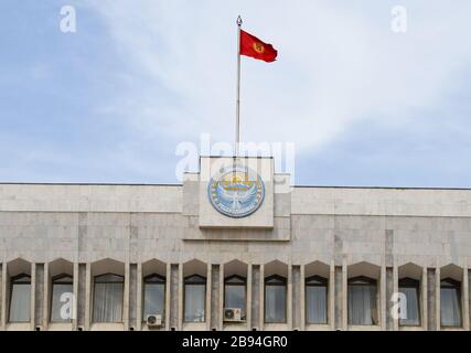 La Casa Bianca del Kirghizistan con l'emblema del governo e il logo Tulip Revolution. Parlamento della Repubblica del Kirghizistan a Bishkek e bandiera. Foto Stock